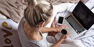A woman holding a cup of coffee while researching CBD products on a laptop