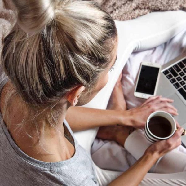A woman holding a cup of coffee while researching CBD products on a laptop
