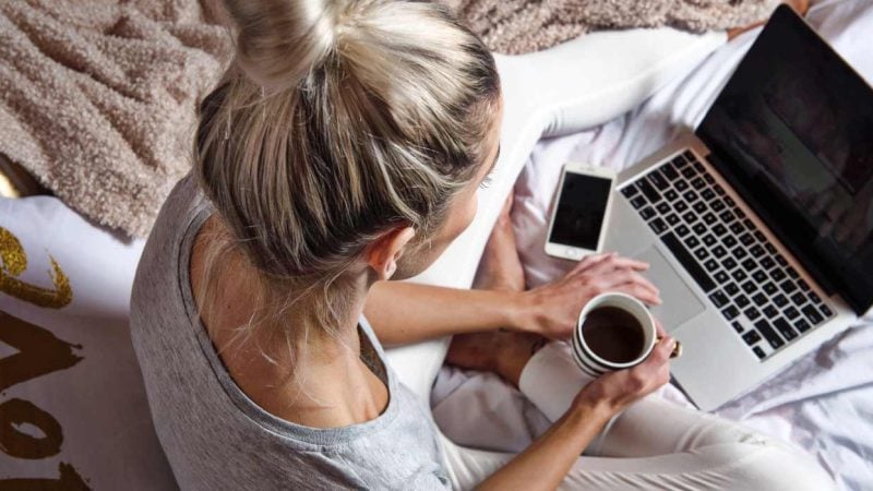 A woman holding a cup of coffee while researching CBD products on a laptop