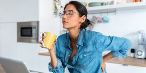 A tired woman with back pain looking uncomfortable as she sits in front of a computer
