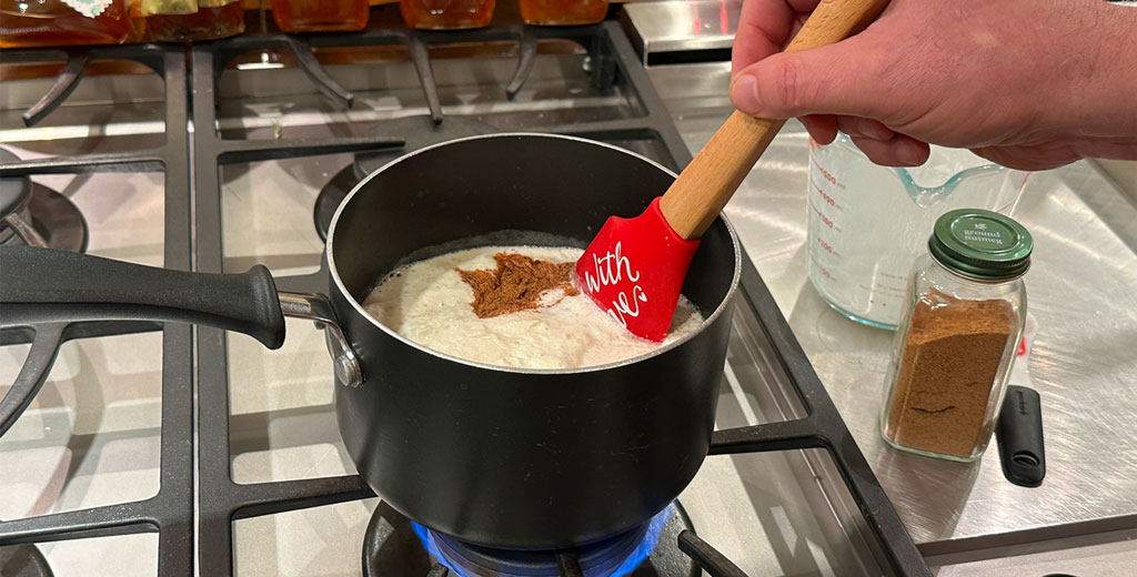 Warming milk, cream, nutmeg, and cinnamon in a saucepan on the stovetop while gently stirring.