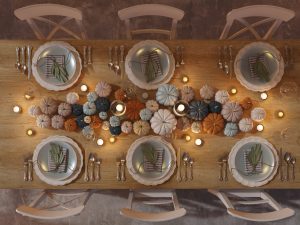Top-down view of an elegant Thanksgiving table setting decorated with neutral and colorful mini pumpkins, candles, and neatly arranged dinner plates for a festive holiday meal.