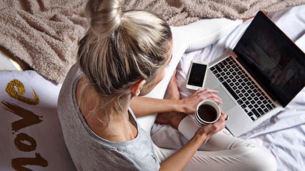 A woman holding a cup of coffee while researching CBD products on a laptop