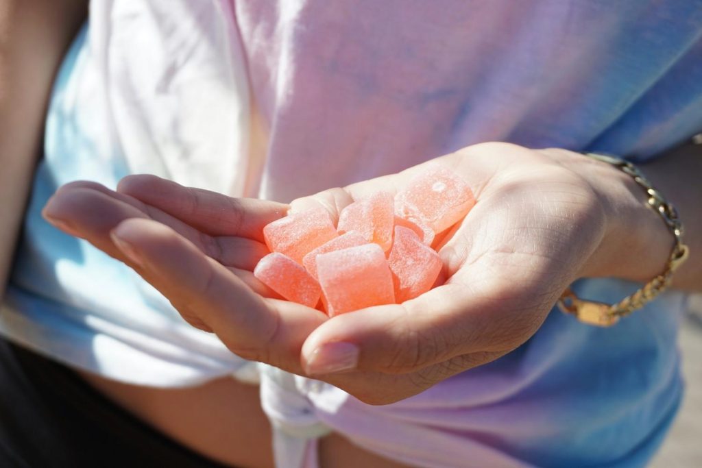 Hand holding orange cannabis gummies, showing consistent size and sugar-coated texture