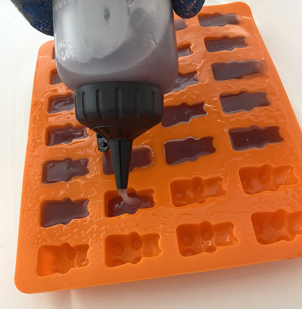 Filling silicone molds with THC gummy mixture from a squeeze bottle for homemade weed edibles.
