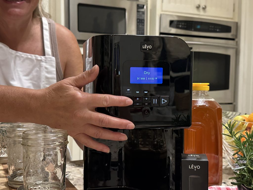 LĒVO infuser pod filled with rosemary leaves and orange peel set to the dry cycle on the countertop.