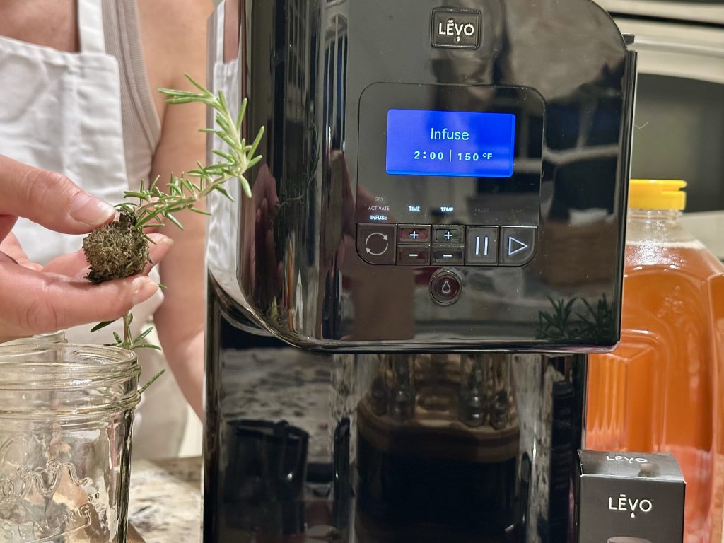 Jar of honey attached to the LĒVO infuser with rosemary, citrus, and decarboxylated cannabis in the pod during the infusion cycle.