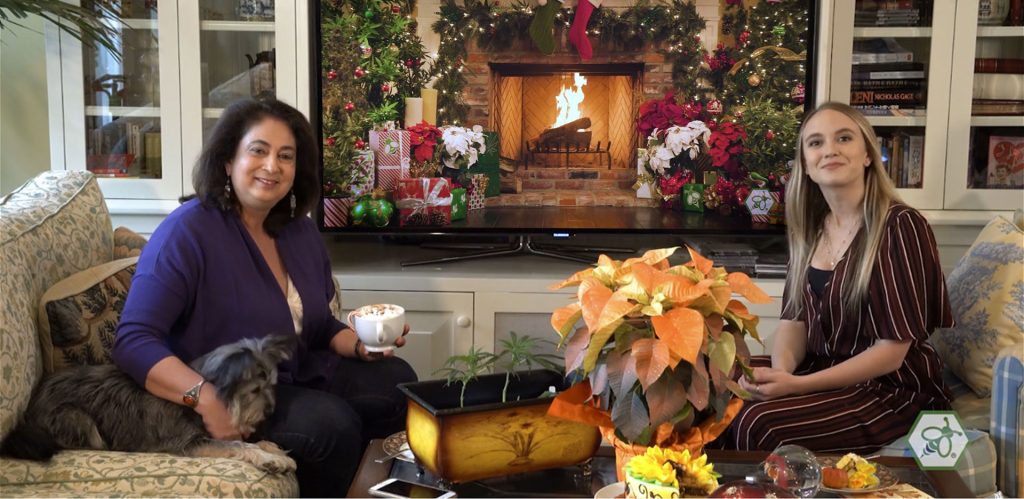 Maria Calabrese and Emily Plizak seated in a living room with the CannaYule Log streaming on a television as a cozy holiday backdrop