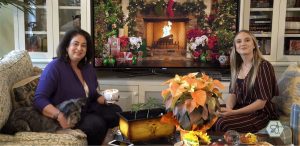 Maria Calabrese and Emily Plizak seated in a living room with the CannaYule Log streaming on a television as a cozy holiday backdrop