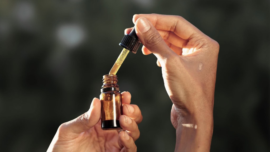 Hands holding a CBD oil dropper bottle.